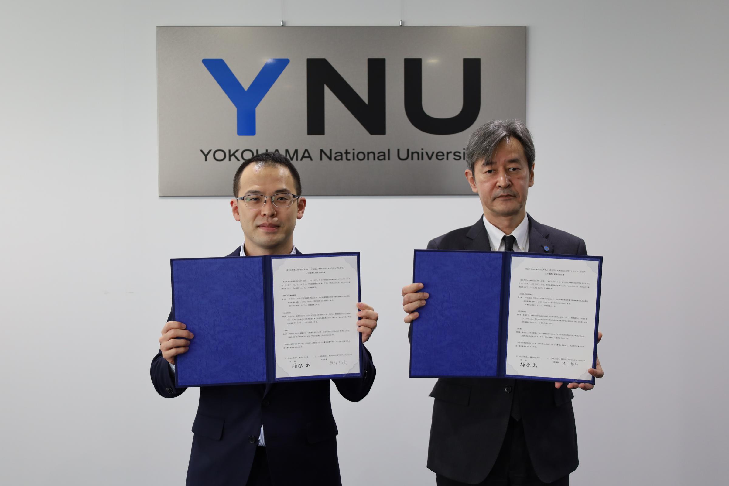 協定書を手にする梅原学長(右)と横川代表理事(左)